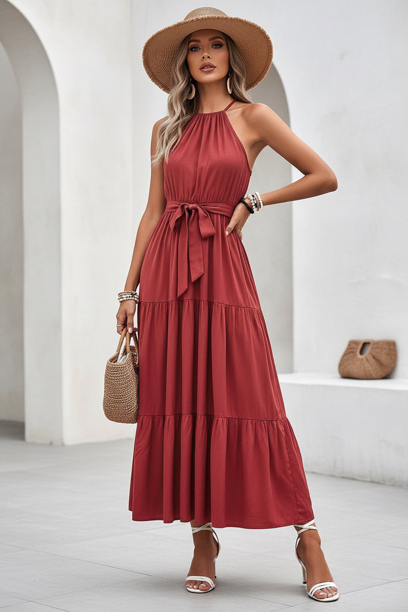 Woman in a red dress sitting on a white wall with a straw bag.