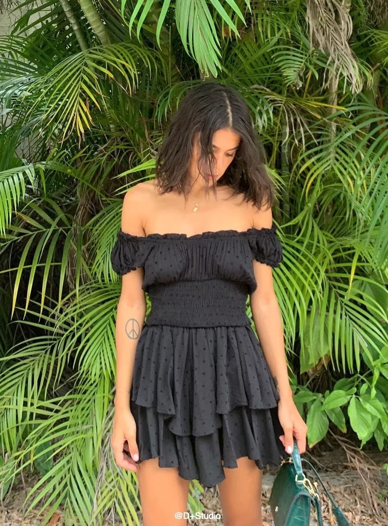 Woman wearing a black off-shoulder dress standing in front of green foliage