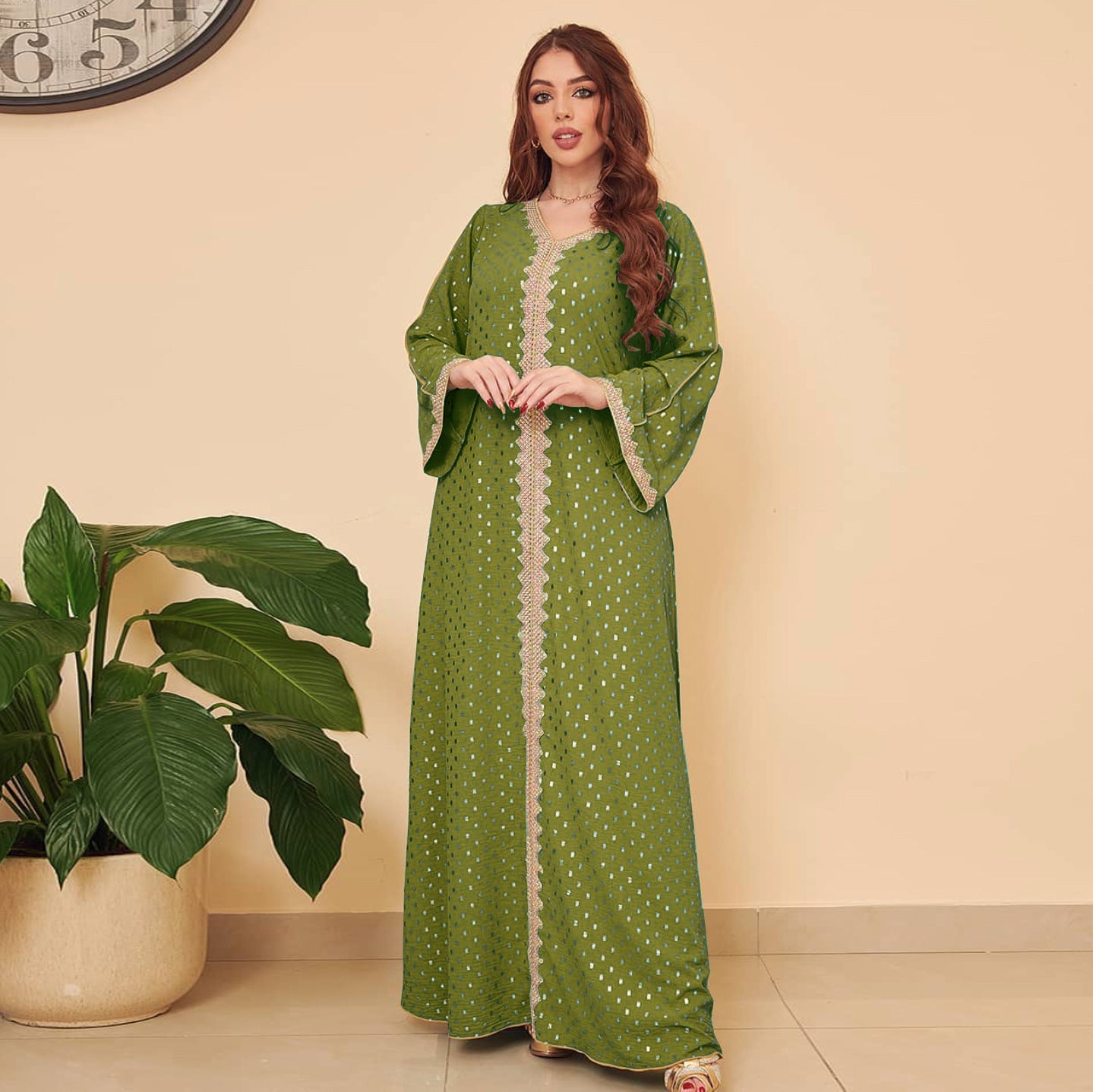 Woman wearing a green dress with white patterns standing next to a plant indoors.
