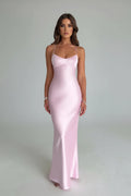 Woman wearing a pink satin dress standing in a minimalistic room with flowers in the background.