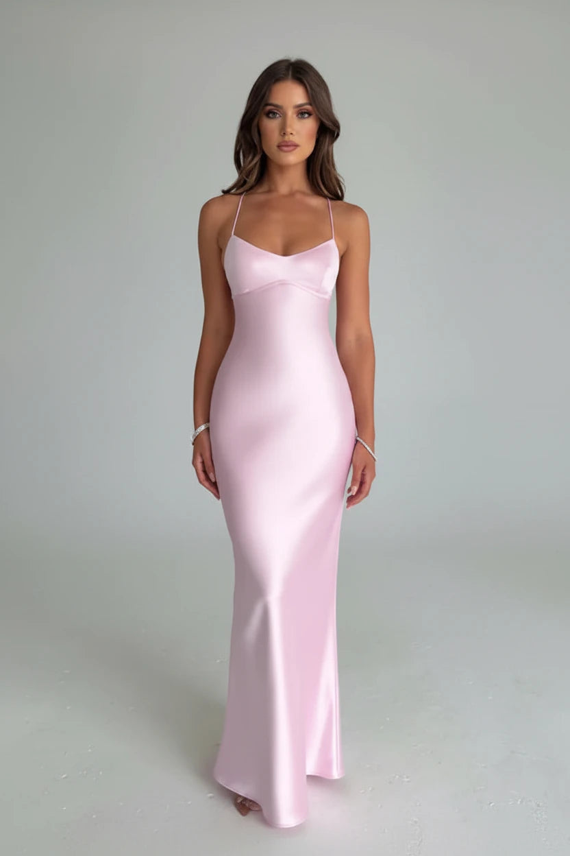 Woman wearing a pink satin dress standing in a minimalistic room with flowers in the background.
