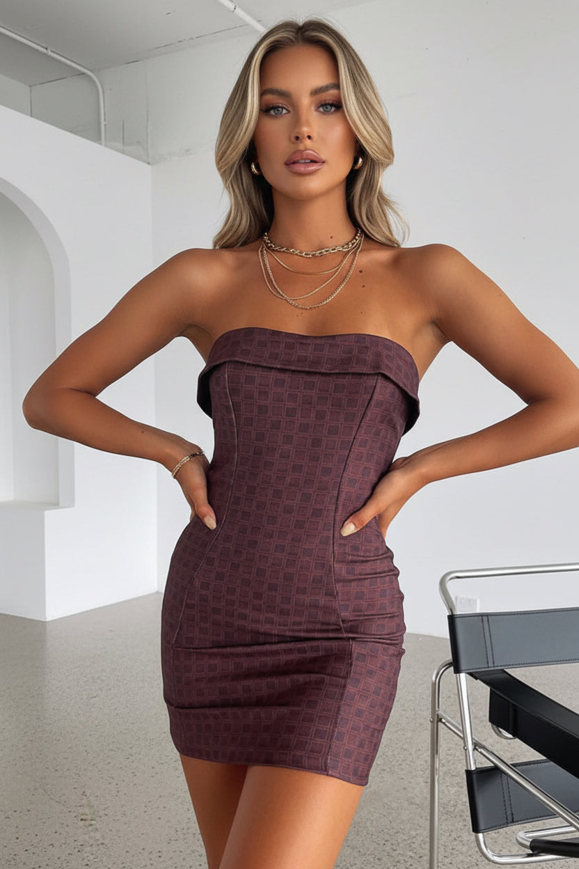 Woman wearing a strapless dress in a minimalistic room with a chair.