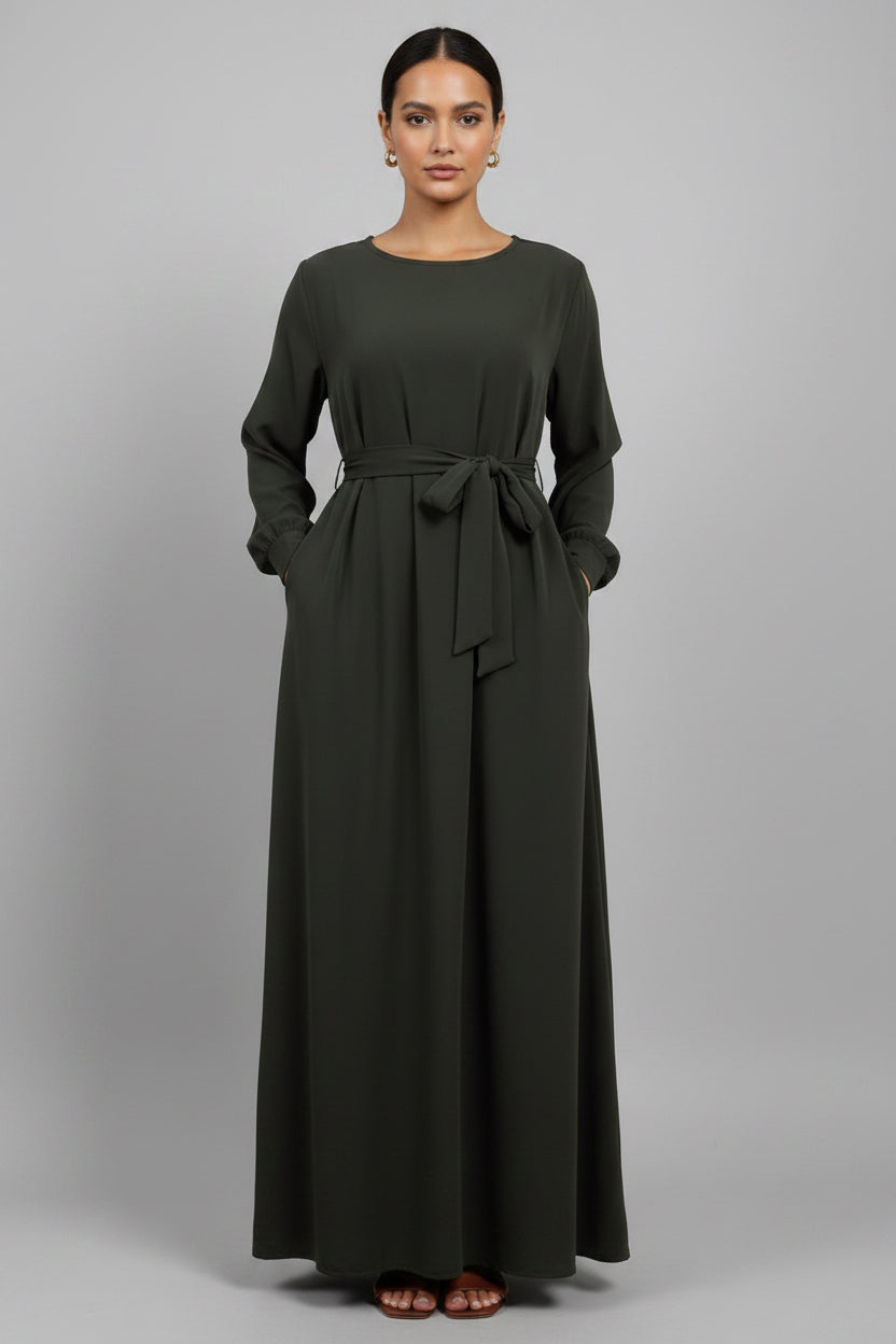 Person wearing a long olive green dress with a belt on a light background