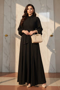 Person wearing a black dress holding a beige handbag in a room with shelves and decor.