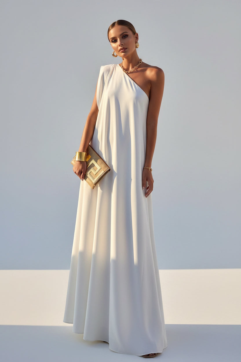 Woman in a white one-shoulder dress standing on a balcony with a scenic view.