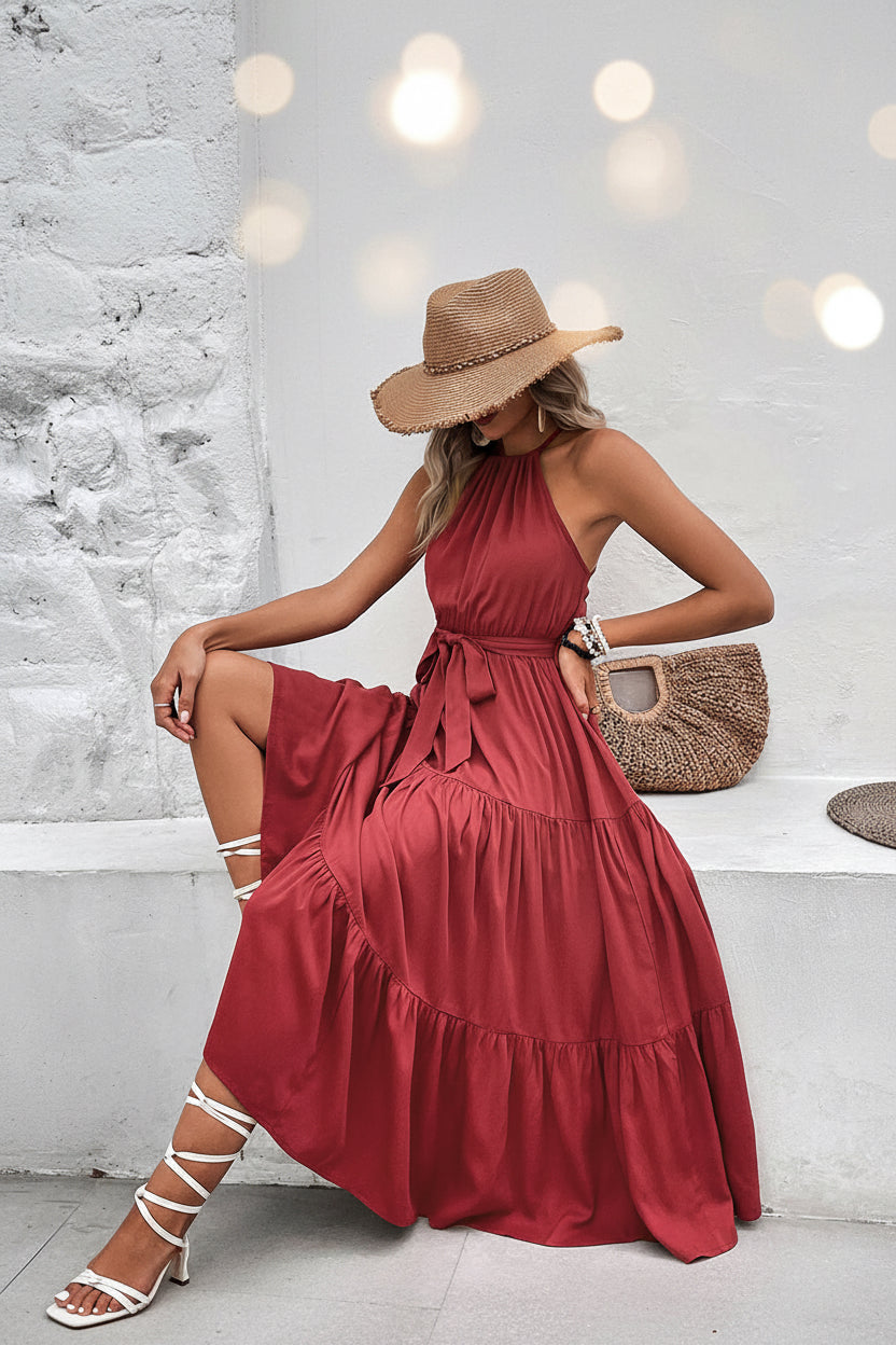 Woman in a red dress sitting on a white wall with a straw bag.