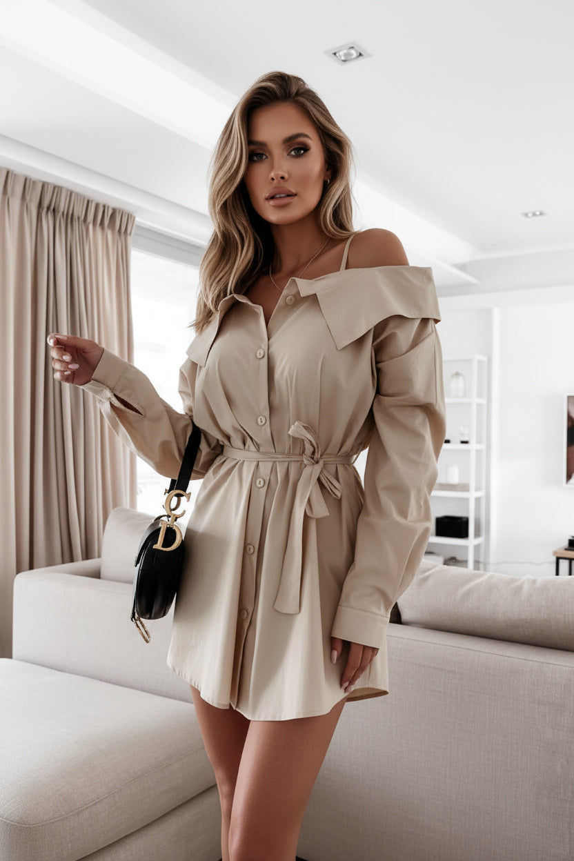 Woman wearing a beige dress holding a black handbag in an indoor setting