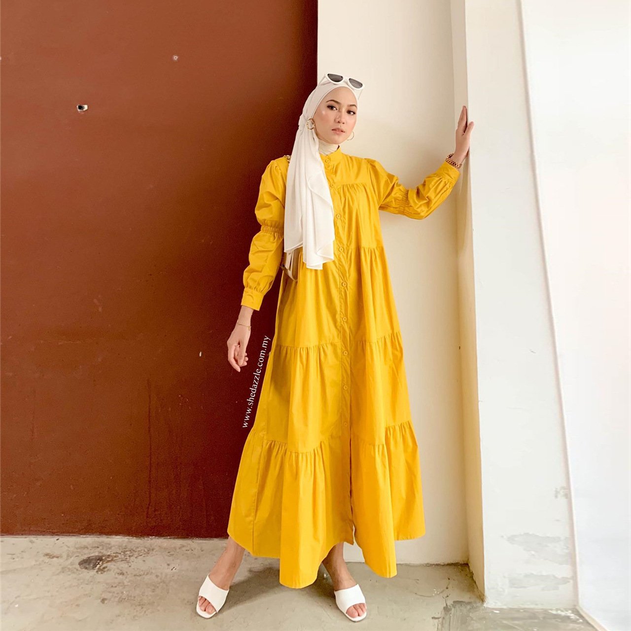 Woman in a yellow dress standing against a red wall.