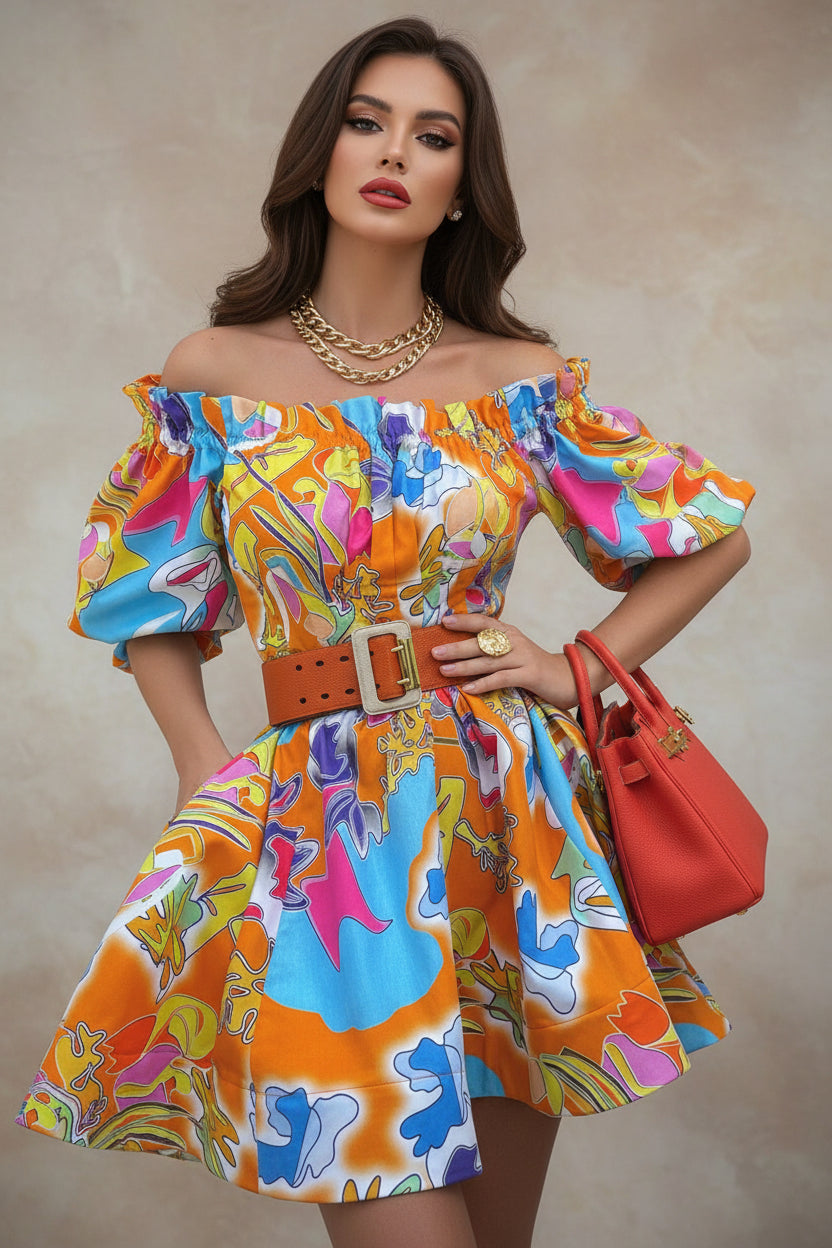 Woman wearing a colorful off-shoulder dress with a red handbag, surrounded by greenery.
