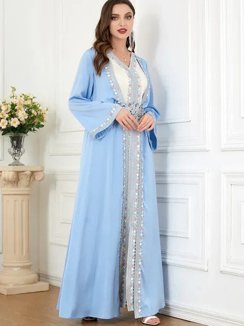 Woman wearing a light blue dress with white embellishments in a room with white walls and a small table with flowers.