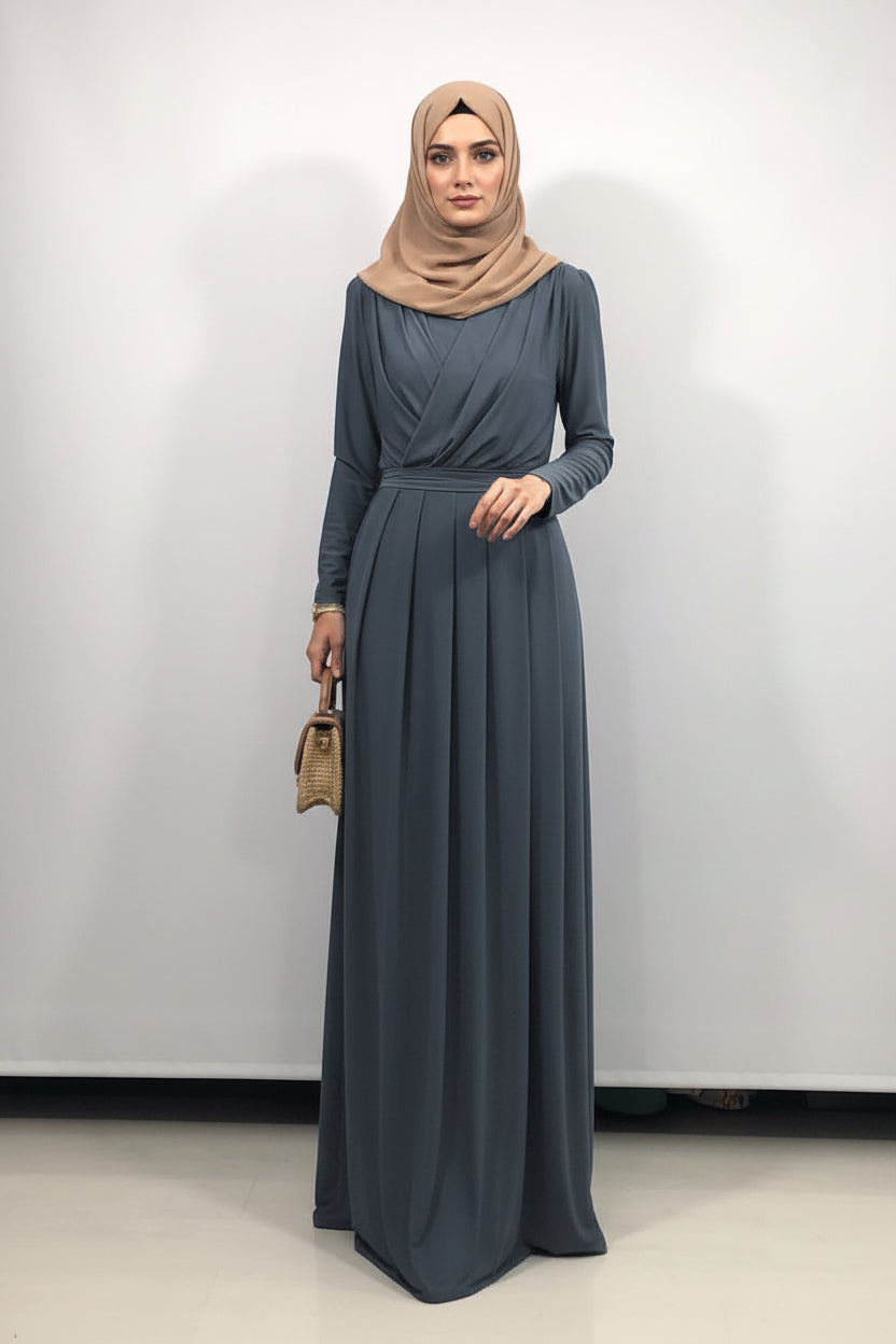 Woman in a long blue dress and hijab taking a mirror selfie.