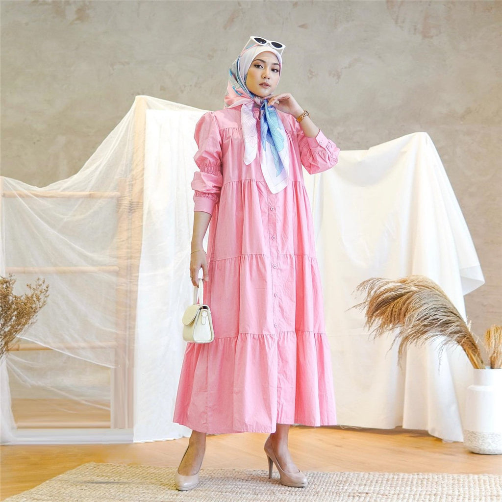 Woman in a pink dress with a headscarf standing in a room with a neutral background