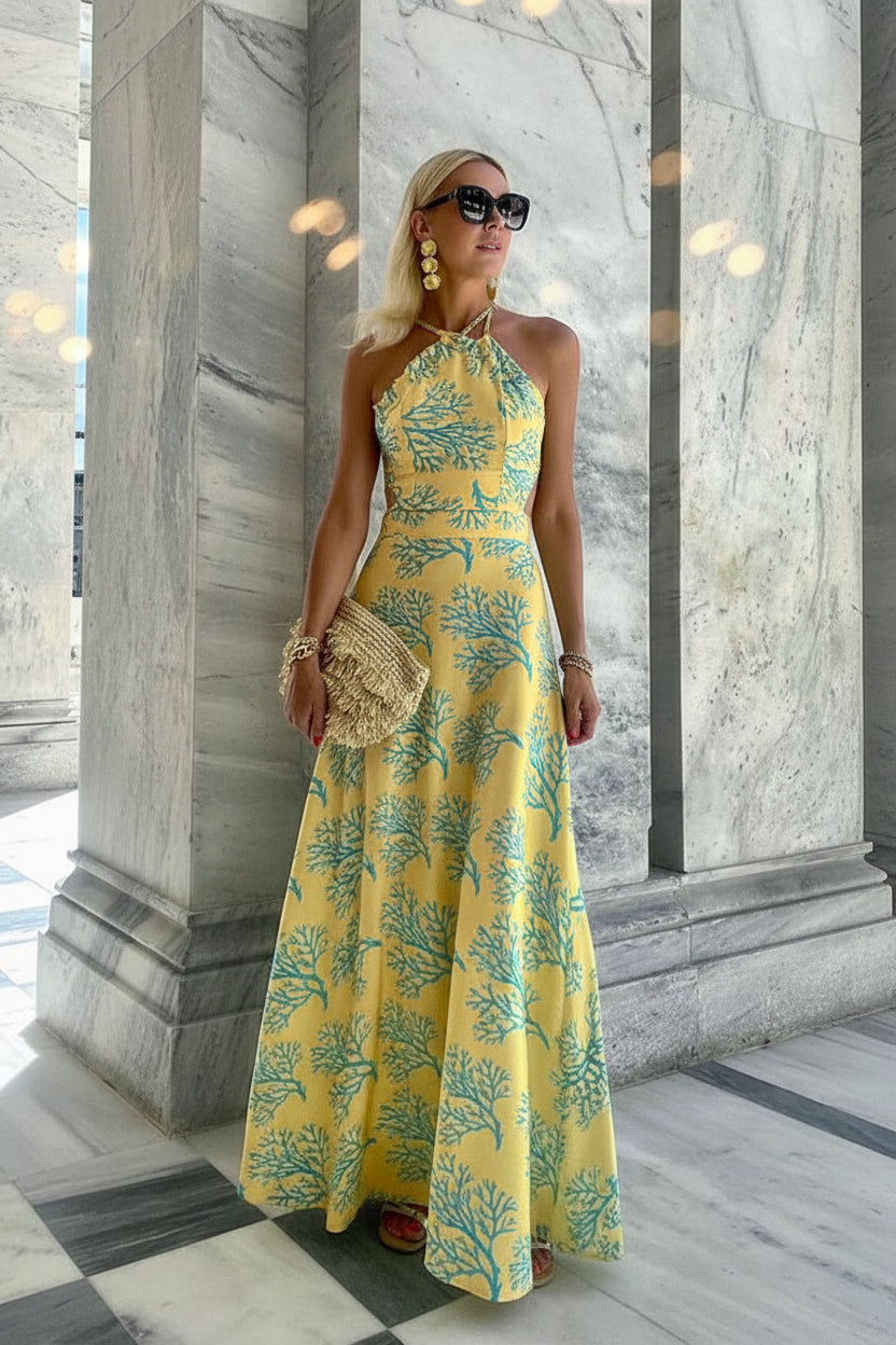 Woman in a yellow floral dress standing in front of a marble wall.