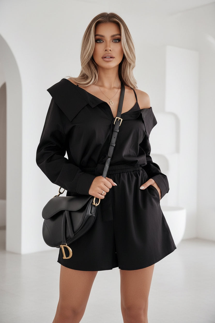 Woman in a black off-shoulder dress holding a matching handbag in a living room.