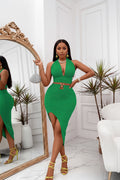 Woman in a green dress posing indoors with a mirror and plant in the background