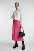 Person wearing a pink skirt and black boots holding a black handbag indoors.