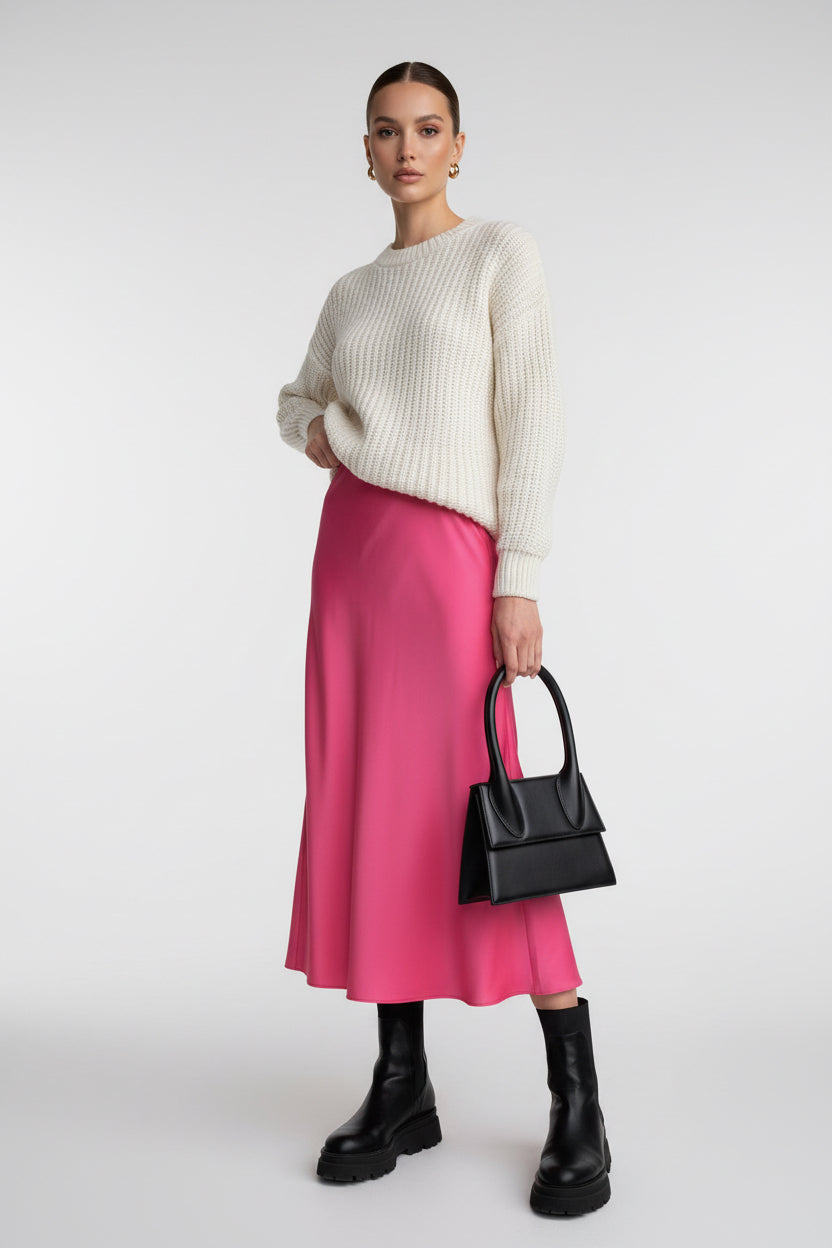 Person wearing a pink skirt and black boots holding a black handbag indoors.