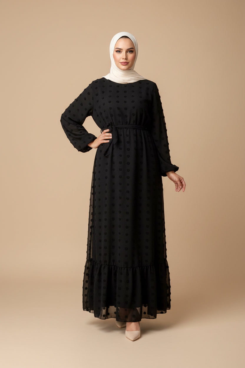 Person wearing a black dress with long sleeves in a bedroom setting.