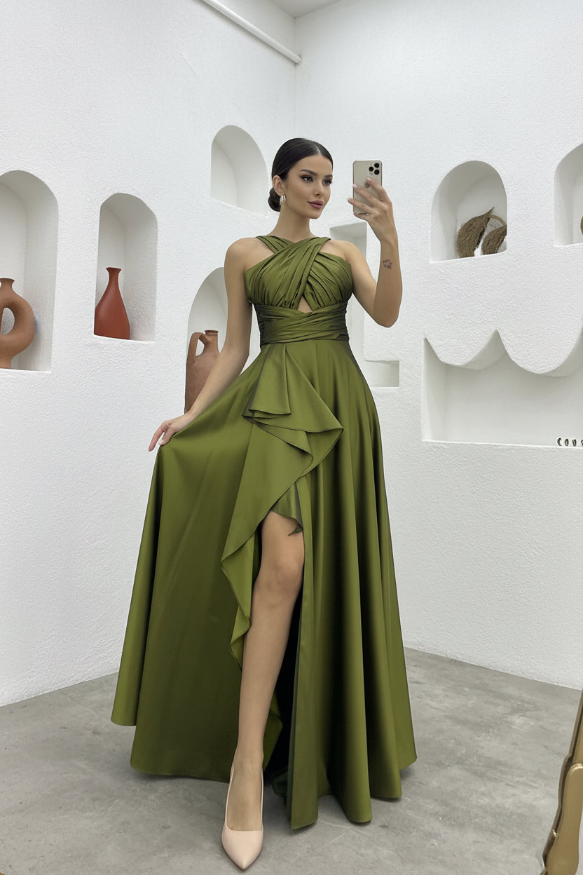Woman in a green evening gown with a high slit, standing against a white wall.