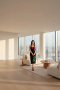 Woman in a red top and black skirt standing on a balcony with a cityscape view.