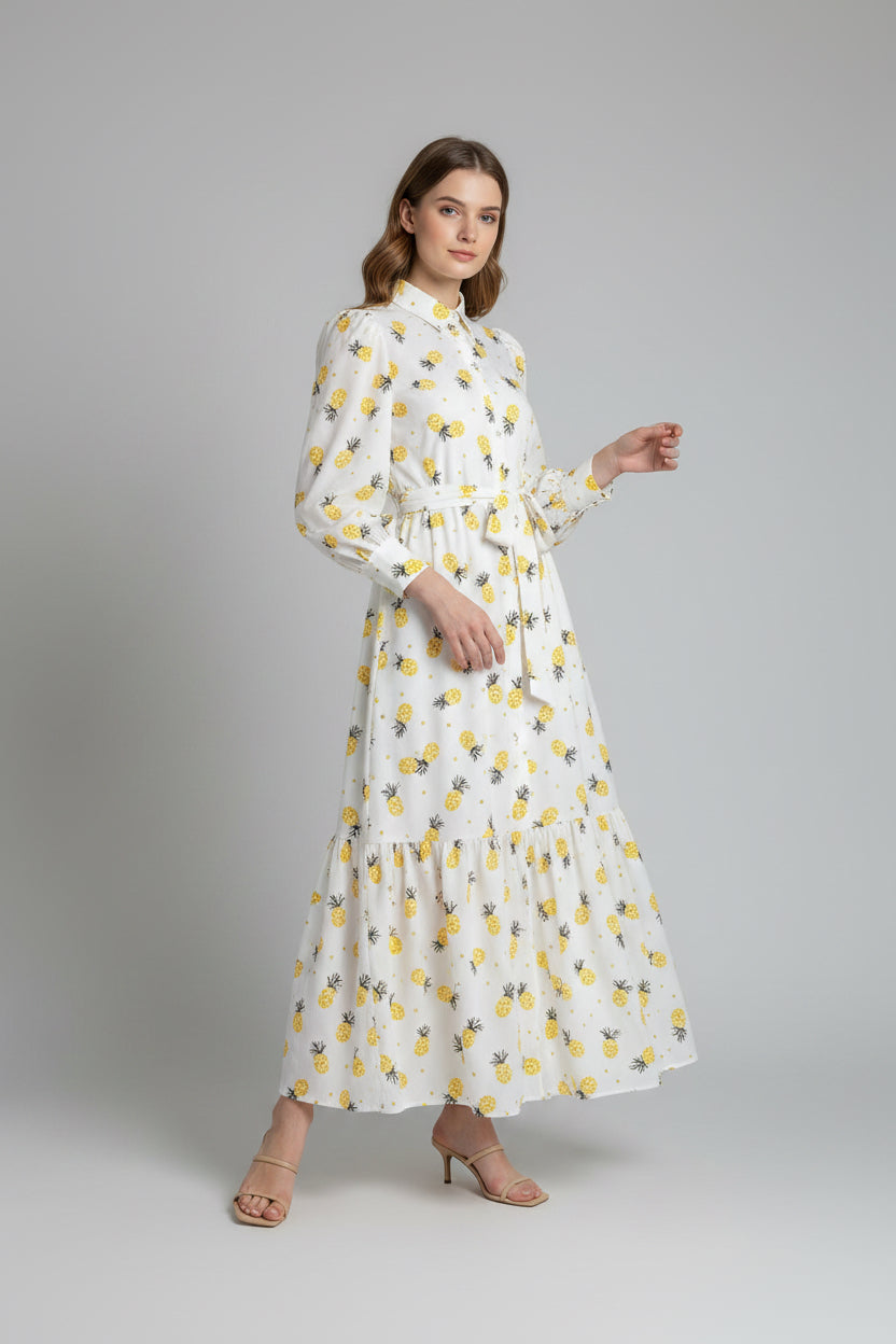 Woman wearing a white dress with yellow pineapple patterns against a plain background