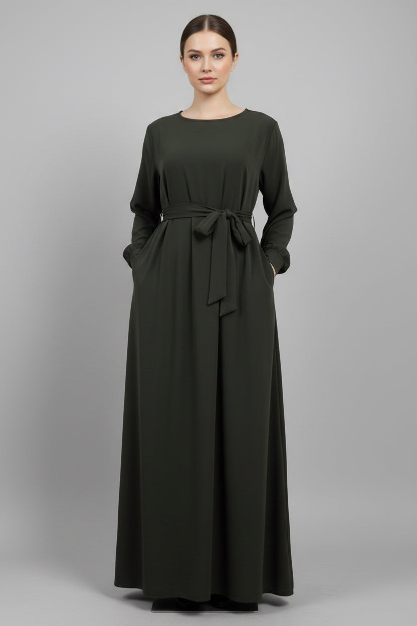 Person wearing a long olive green dress with a belt on a light background