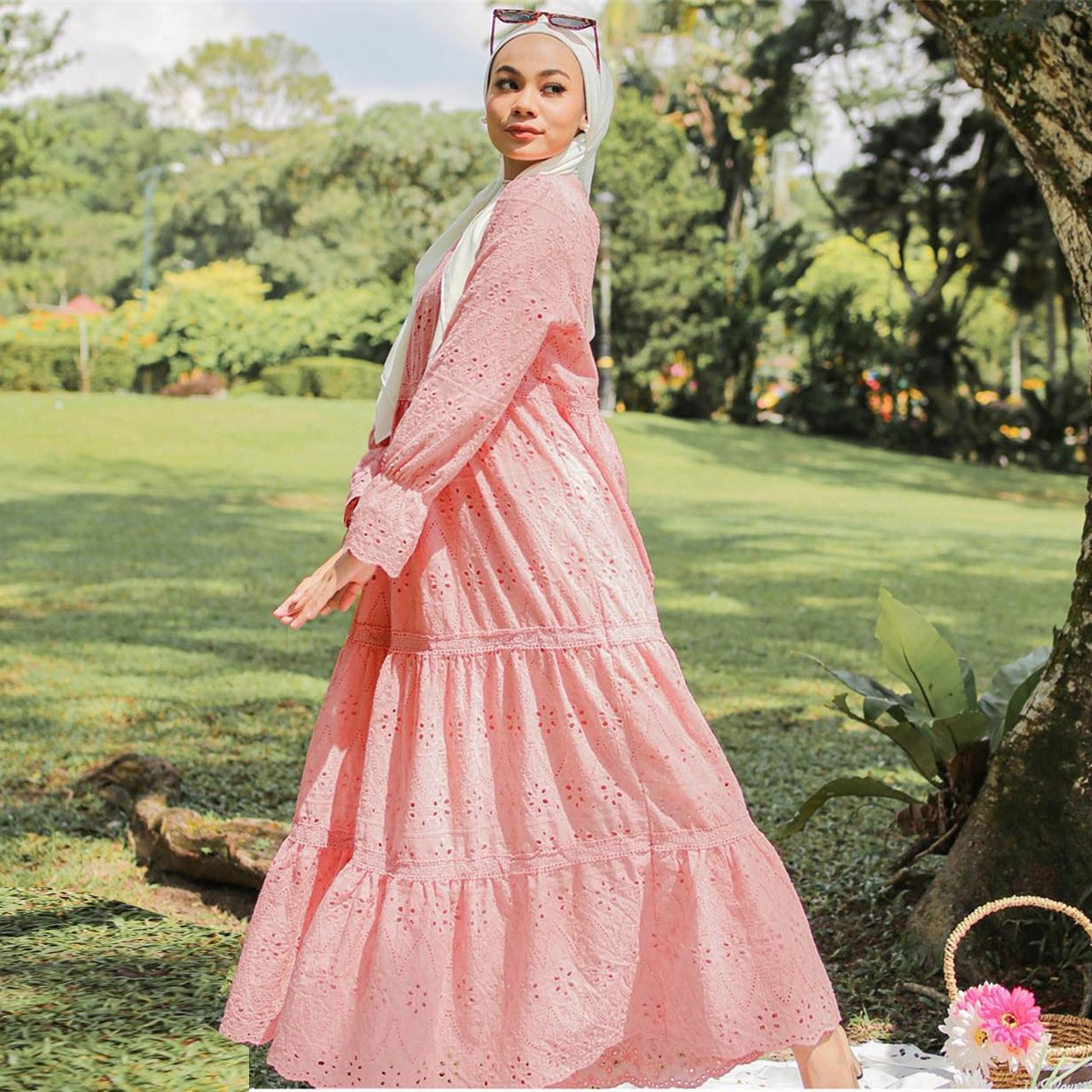 Woman in a pink dress standing in a park with trees and grass in the background