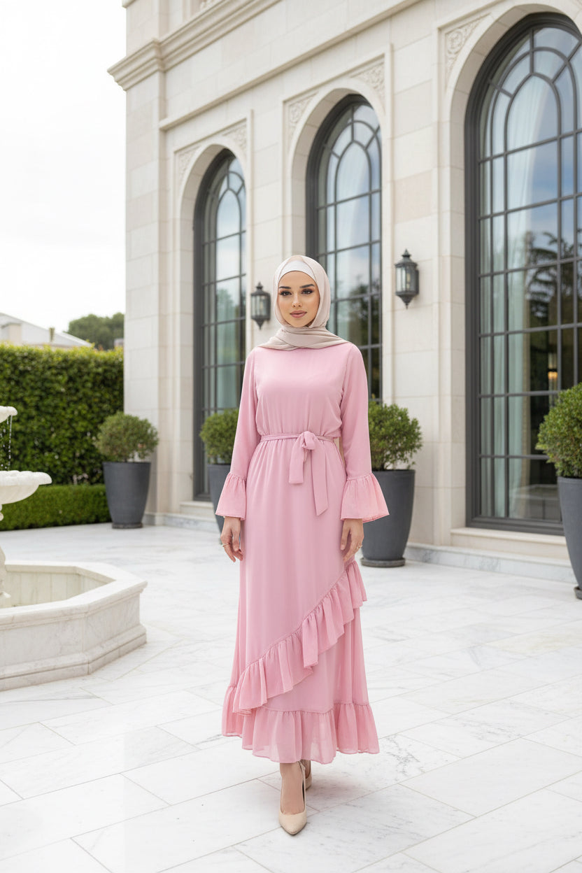 Woman in a pink dress standing outside a building with a brick wall and wooden door.