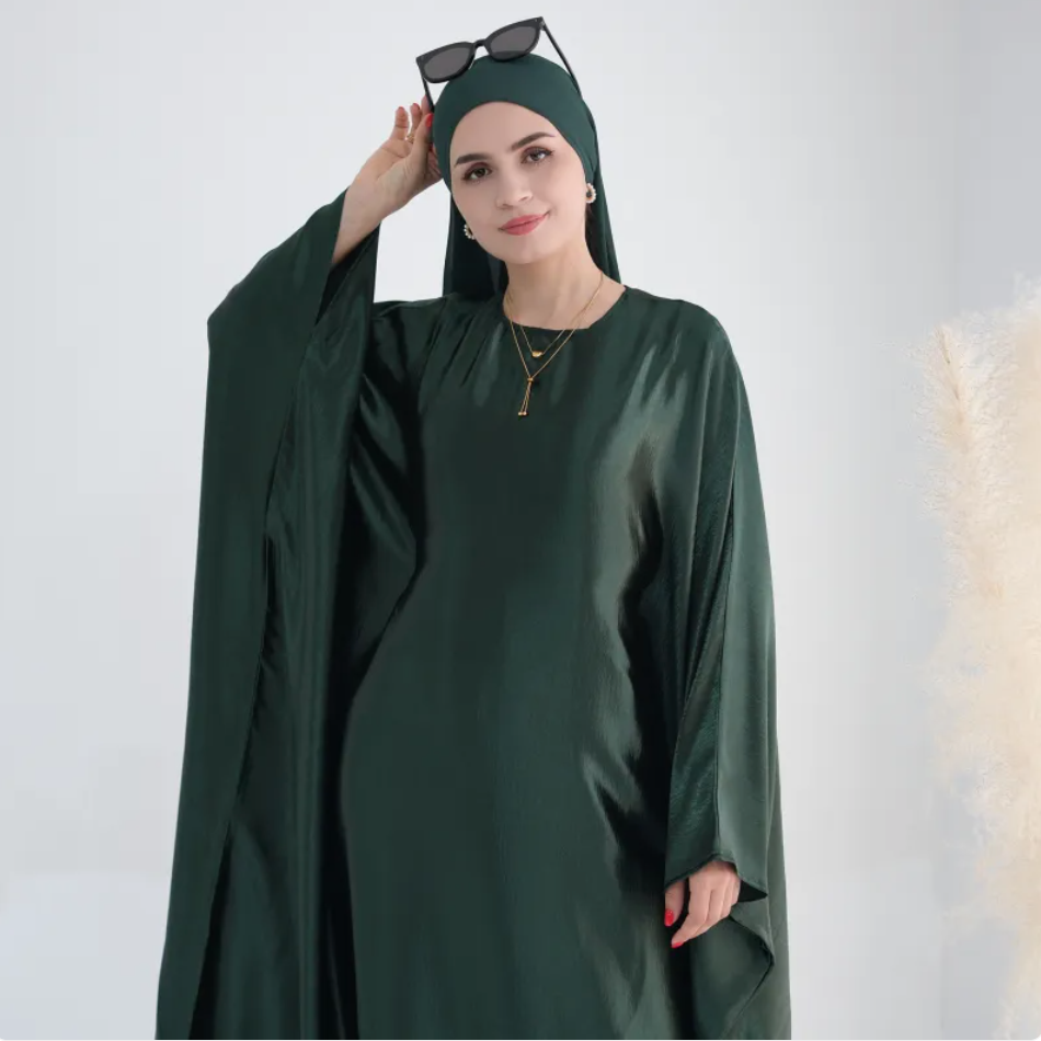 Woman wearing a dark green abaya with sunglasses on her head against a white background