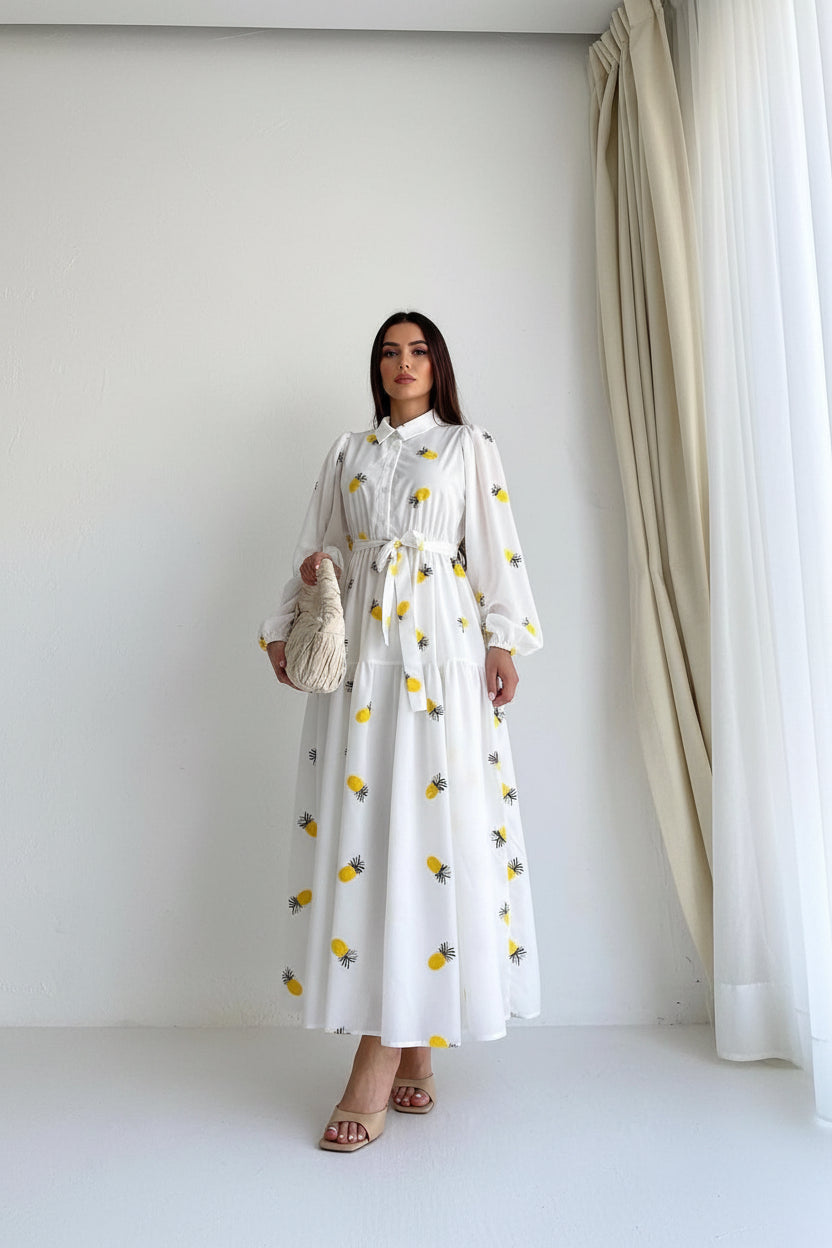 Woman wearing a white dress with yellow pineapple patterns against a plain background