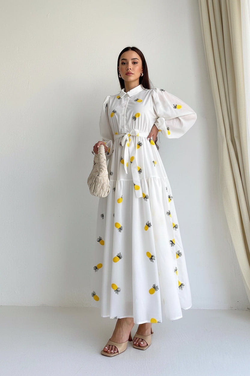 Woman wearing a white dress with yellow pineapple patterns against a plain background