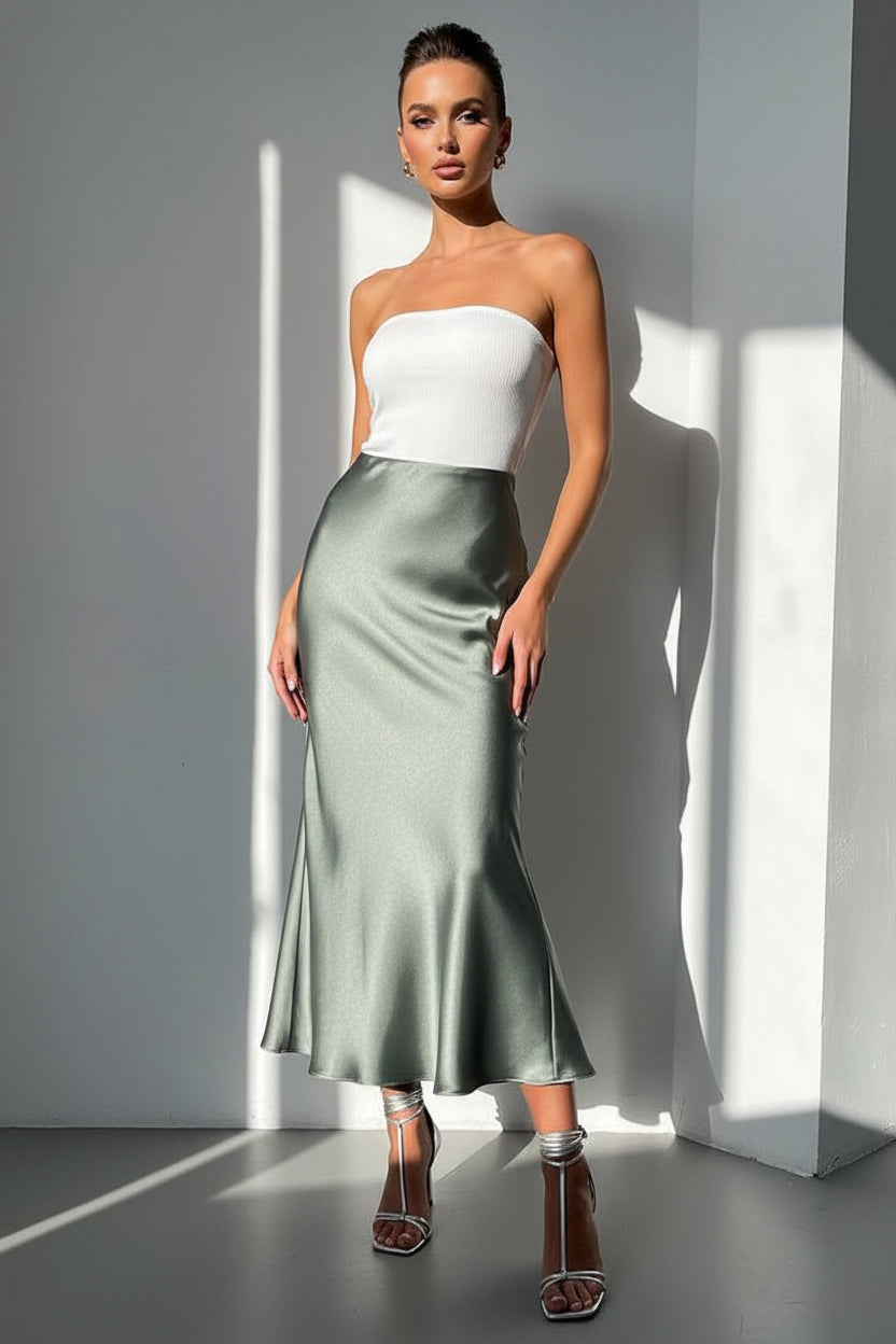Person wearing a green satin skirt and silver strappy sandals on a light gray floor.