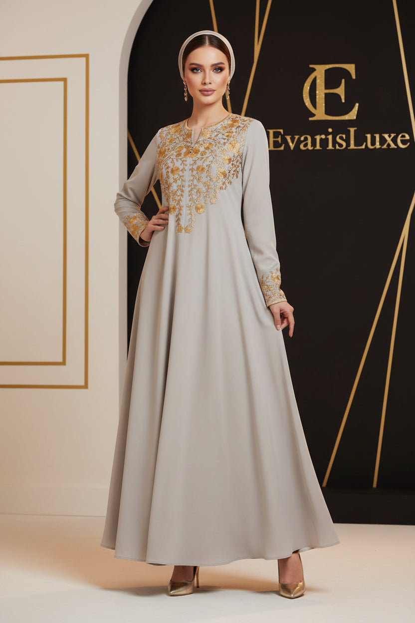 Woman wearing a long, light-colored dress with gold embroidery in an outdoor setting.